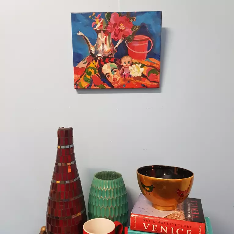 An exotic scarf printed with a Gustave Klimt painting is reflected in a silver teapot. A kewpie doll and some bright flowers…