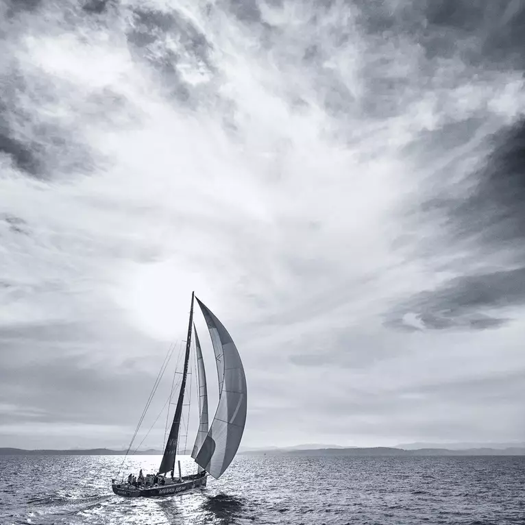 A racing yacht sails on glittering silver water beneath a towering swirling cloudy sky during the Sydney to Hobart Yacht Rac…