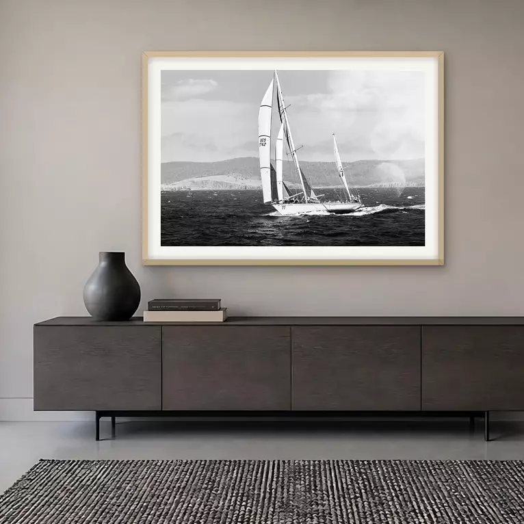 Three racing yachts with tall white sails move together across glittering water in hazy light during the Sydney to Hobart Ya…