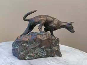 Small realistic sculpture of a dog crawling over rocks.
