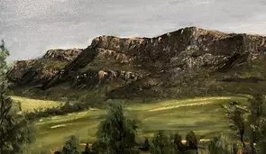 Rugged mountains in background with green field and trees in foreground.