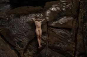 pixelated man in a sculptural pose on a coastal rock formation