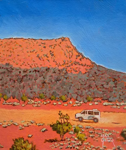 Our white van travels along a dirt road, past an orange mesa in outback Australia.